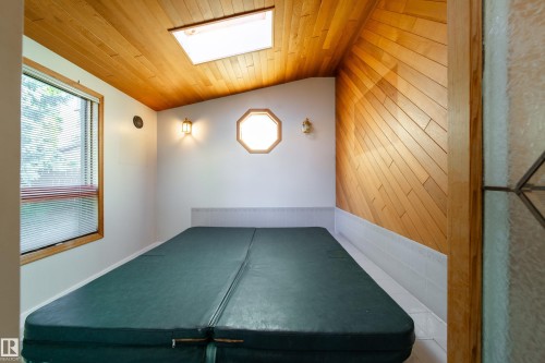 Sloped wood-paneled ceiling with skylight, wood-paneled wall, rectangular window with blinds, octagonal window, and wall-mounted light fixtures - 10438 32A Avenue Nw, Edmonton, AB 