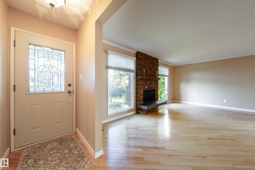 Entryway with decorative glass door, leading to a living area featuring wood-finish flooring, a brick fireplace, and multiple windows - 10438 32A Avenue Nw, Edmonton, AB 