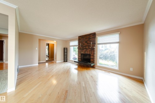 Spacious area with light wood-finish flooring, a brick-surround fireplace with a dark hearth, large windows, and neutral wall tones - 10438 32A Avenue Nw, Edmonton, AB 