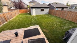Expansive green space featuring a wood-plank deck, privacy fencing, and a detached structure with siding - 