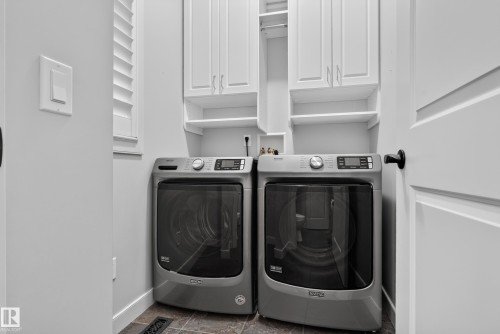 Laundry area featuring dual front-load appliances, upper cabinetry, open shelving, and tiled flooring - 904 Armitage Court Sw, Edmonton, AB 