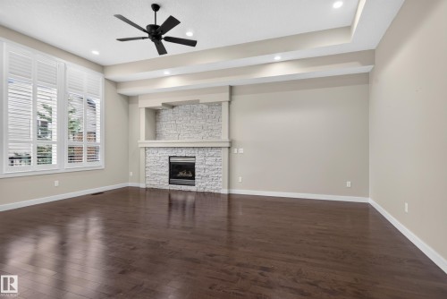 Dark wood-finish flooring with a gas fireplace featuring a stacked stone surround - 904 Armitage Court Sw, Edmonton, AB 