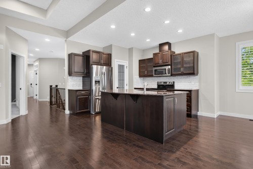 Open-concept kitchen with dark wood cabinetry, stainless steel appliances, a large center island with a sink, and recessed lighting - 904 Armitage Court Sw, Edmonton, AB 