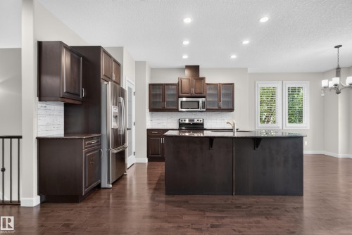 Kitchen featuring dark wood cabinetry, stainless steel appliances, a central island with an undermount sink, a subway tile backsplash, and recessed lighting - 904 Armitage Court Sw, Edmonton, AB 