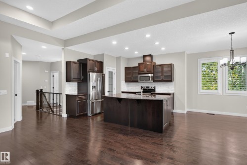 Kitchen featuring wood-finish flooring, dark wood cabinetry, stainless steel appliances, a center island with sink, and a tiled backsplash - 904 Armitage Court Sw, Edmonton, AB 