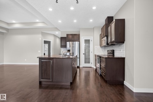 Kitchen featuring dark wood-finish cabinetry, stainless steel appliances, a center island with sink, and a white subway tile backsplash - 904 Armitage Court Sw, Edmonton, AB 