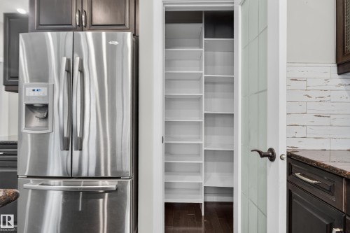 Stainless steel refrigerator, dark wood-finish cabinetry, built-in pantry shelving, paneled interior door, and a white wood-finish accent wall - 904 Armitage Court Sw, Edmonton, AB 