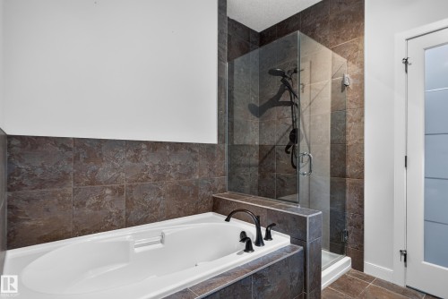 Soaking tub with bronze fixtures, glass-enclosed shower, and coordinating wall and floor tiles - 904 Armitage Court Sw, Edmonton, AB 