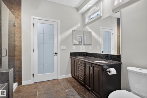 Dual vanity with dark cabinetry and countertop, tiled flooring, glass-enclosed shower, and transom windows - 904 Armitage Court Sw, Edmonton, AB 