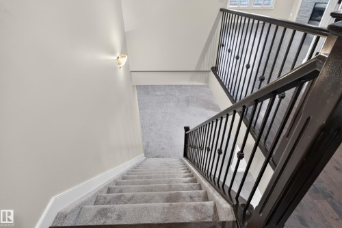 Carpeted staircase with dark wood-finish handrails and wrought iron balusters, complemented by a wall-mounted sconce - 904 Armitage Court Sw, Edmonton, AB 