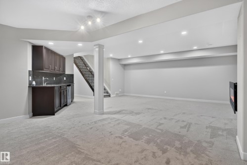 Recessed lighting, built-in wet bar with dark cabinetry, integrated mini-refrigerator, wall-mounted electric fireplace, and light gray carpeting - 904 Armitage Court Sw, Edmonton, AB 