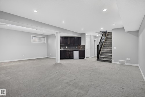 Spacious interior with recessed lighting, dark wood-finish cabinetry, a built-in sink, and a carpeted staircase with dark railings - 904 Armitage Court Sw, Edmonton, AB 