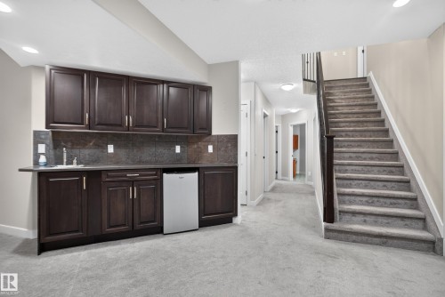 Wet bar with dark wood cabinetry, integrated sink, and stainless steel compact refrigerator - 904 Armitage Court Sw, Edmonton, AB 