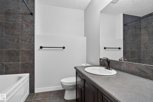 Bathroom featuring a shower-tub combination with dark tile surround, a single vanity with an integrated sink, a dark wood-finish cabinet, and a large wall-mounted mirror - 904 Armitage Court Sw, Edmonton, AB 
