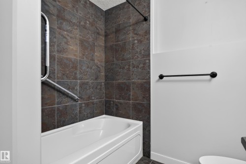 Full-height tile bath surround, white tub, matte black shower rod, and a coordinating towel bar - 904 Armitage Court Sw, Edmonton, AB 