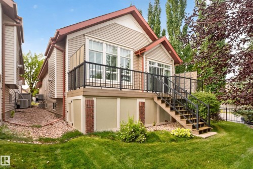 Expansive rear yard with a manicured lawn, a multi-level deck featuring dark railings, a sliding glass door, and exterior siding with brick accents - 904 Armitage Court Sw, Edmonton, AB 