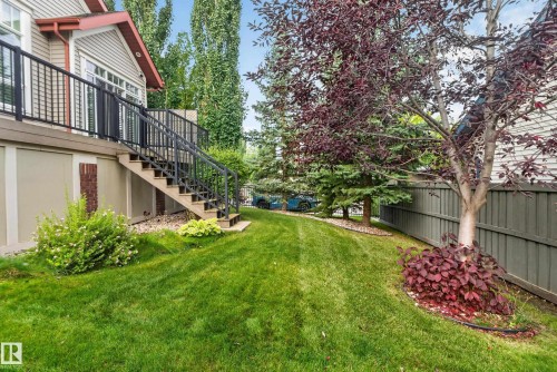 Expansive lawn with mature trees and established landscaping, featuring a raised deck with metal railings and exterior stairs - 904 Armitage Court Sw, Edmonton, AB 