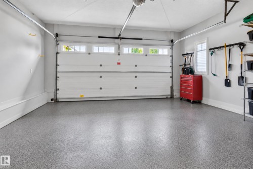 Attached garage featuring an epoxy-coated floor, overhead garage door with transom windows, and a side window with horizontal blinds - 904 Armitage Court Sw, Edmonton, AB 