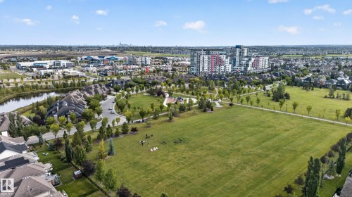 Expansive green spaces with mature trees and paved pathways, complemented by a nearby pond and residential structures - 904 Armitage Court Sw, Edmonton, AB 
