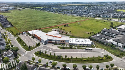 Aerial perspective showcasing a large green space, surrounding residential developments, a modern institutional building, and established roadways - 904 Armitage Court Sw, Edmonton, AB 