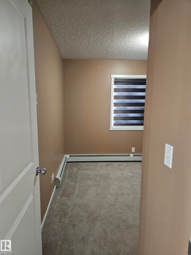 Neutral-toned walls, textured ceiling, gray carpeting, window with horizontal blinds, and baseboard heating - #421 5816 Mullen Place Nw, Edmonton, AB 