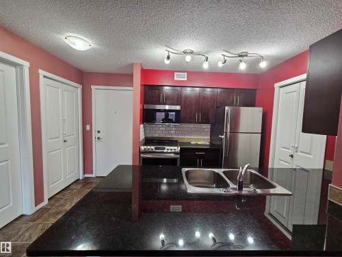 Kitchen with dark wood-finish cabinetry, stainless steel appliances, dark speckled countertops, and a subway tile backsplash - #421 5816 Mullen Place Nw, Edmonton, AB 