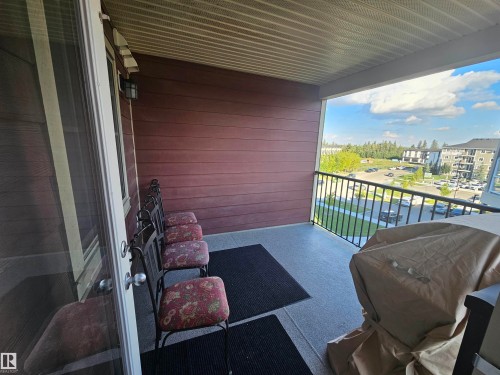 Covered balcony with a textured ceiling, a textured wall, and a black metal railing - #421 5816 Mullen Place Nw, Edmonton, AB 