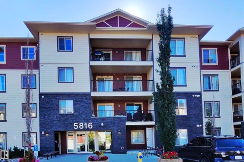 Contemporary multi-story building with a facade featuring cream-colored siding, maroon-colored siding, and dark stacked stone accents - #421 5816 Mullen Place Nw, Edmonton, AB 
