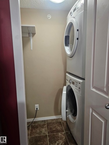 Stackable washer and dryer unit, tiled flooring, built-in shelving, and overhead lighting - #421 5816 Mullen Place Nw, Edmonton, AB 