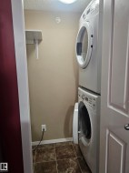 Stackable washer and dryer unit, tiled flooring, built-in shelving, and overhead lighting - 