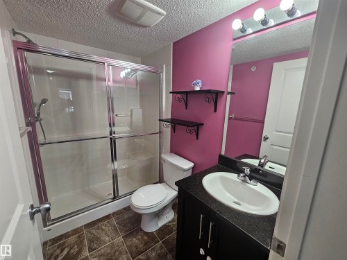 Enclosed shower with sliding glass doors, a vanity with a white oval sink, and a large wall-mounted mirror with overhead lighting - #421 5816 Mullen Place Nw, Edmonton, AB 