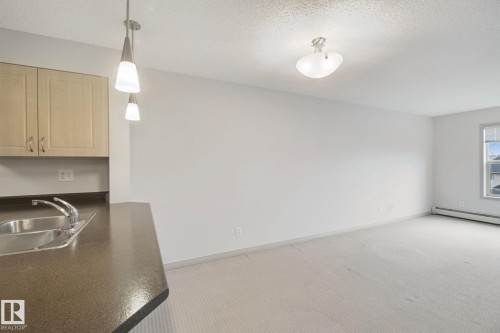 Kitchen counter with integrated stainless steel sink, pendant lighting, and light wood cabinetry - #406 11449 Ellerslie Rd Sw, Edmonton, AB 