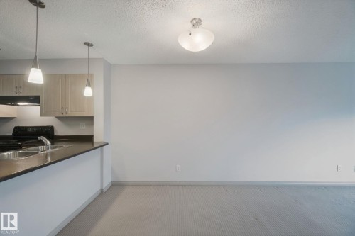 Kitchen with a dual-basin sink, black range, and light wood-finish cabinetry - #406 11449 Ellerslie Rd Sw, Edmonton, AB 