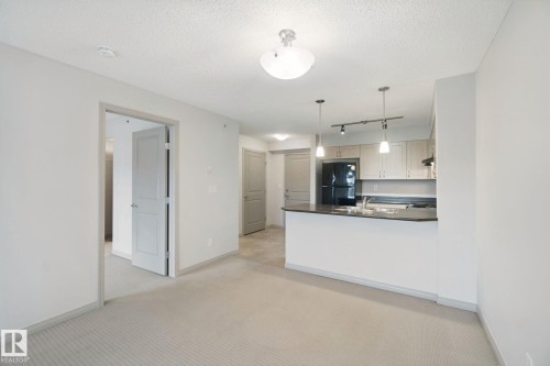 Kitchen island with a dark countertop and pendant lighting - #406 11449 Ellerslie Rd Sw, Edmonton, AB 