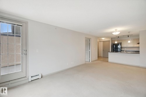 Open-concept living space featuring a kitchen with light wood-finish cabinetry, black appliances, and pendant lighting - #406 11449 Ellerslie Rd Sw, Edmonton, AB 