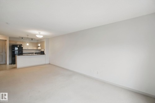 Carpeted living area with a kitchen featuring wood-finish cabinetry, black appliances, a peninsula, and recessed lighting - #406 11449 Ellerslie Rd Sw, Edmonton, AB 
