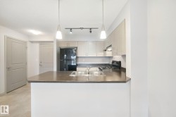 Kitchen featuring light wood-finish cabinetry, dark countertops, a double basin stainless steel sink, and pendant lighting - 