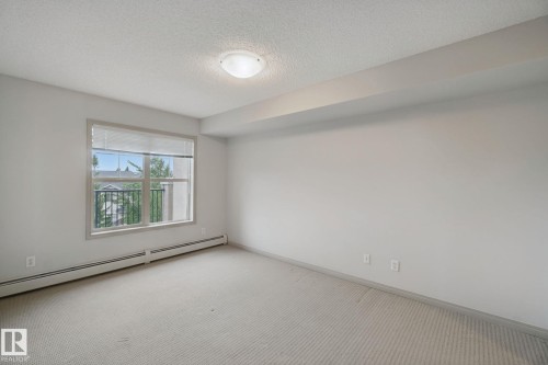 Neutral wall finishes, textured ceiling, window with blinds, and wall-to-wall carpeting - #406 11449 Ellerslie Rd Sw, Edmonton, AB 