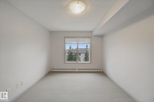 Neutral wall finishes, textured ceiling, window with blinds, baseboard heating, and ceiling-mounted light fixture - #406 11449 Ellerslie Rd Sw, Edmonton, AB 