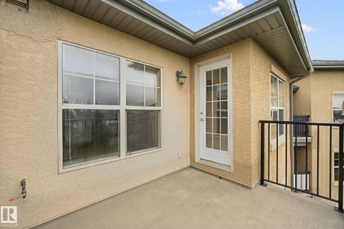 Private balcony with textured stucco exterior, white paneled door, and black metal railing - #406 11449 Ellerslie Rd Sw, Edmonton, AB 