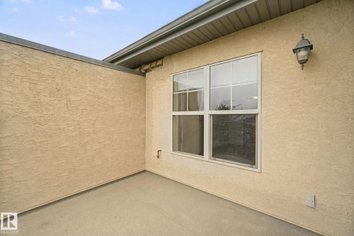 Textured stucco exterior with a covered patio area, featuring a multi-pane window and an exterior wall lantern - #406 11449 Ellerslie Rd Sw, Edmonton, AB 