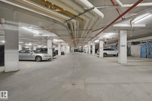 Underground parking garage featuring concrete flooring, structural pillars, and overhead utility lines - #406 11449 Ellerslie Rd Sw, Edmonton, AB 