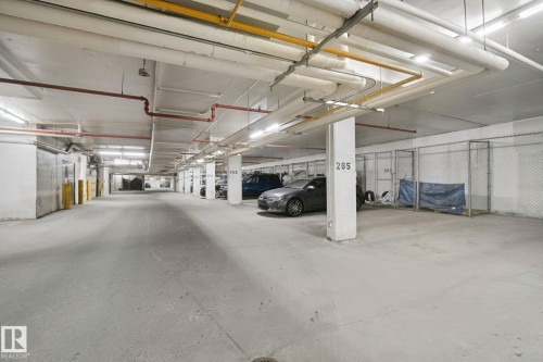 Underground parking facility featuring concrete flooring, overhead lighting, and dedicated storage units - #406 11449 Ellerslie Rd Sw, Edmonton, AB 