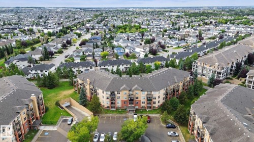 Aerial view of a brick and stone mid-rise residential complex featuring multiple units arranged around a central courtyard with mature landscaping, surface parking, and tree-lined surroundings - #406 11449 Ellerslie Rd Sw, Edmonton, AB 