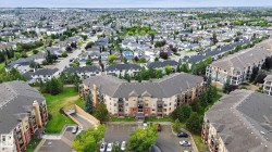 Aerial view of a brick and stone mid-rise residential complex featuring multiple units arranged around a central courtyard with mature landscaping, surface parking, and tree-lined surroundings - 