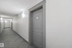Hallway featuring wall sconces, patterned carpet flooring, and a paneled entry door with substantial trim - 
