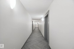 Long hallway with light gray walls, textured ceiling, a patterned carpet runner, and wall-mounted sconces - 