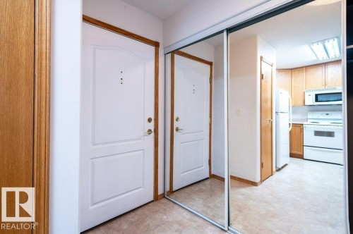 White paneled entry door with wood-finish trim, mirrored sliding closet doors, and tile flooring - #203 8912 156 St Nw, Edmonton, AB 