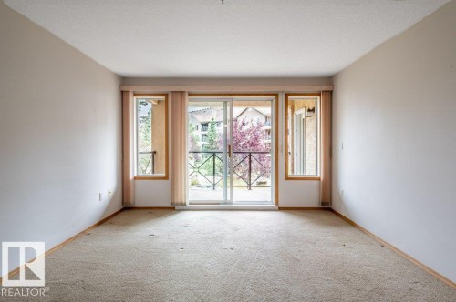 Spacious living room with Sliding glass door leading to a private balcony space, flanked by two side windows, and finished with light-toned wall-to-wall carpeting - #203 8912 156 St Nw, Edmonton, AB 