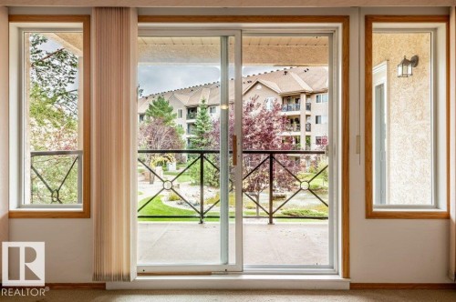 Sliding glass patio door with wood-trim windows, opening to a private balcony with decorative metal railing - #203 8912 156 St Nw, Edmonton, AB 